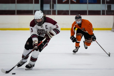 carries the puck through the neutral zone, trailed by Plattsburgh's Hunter Broadway